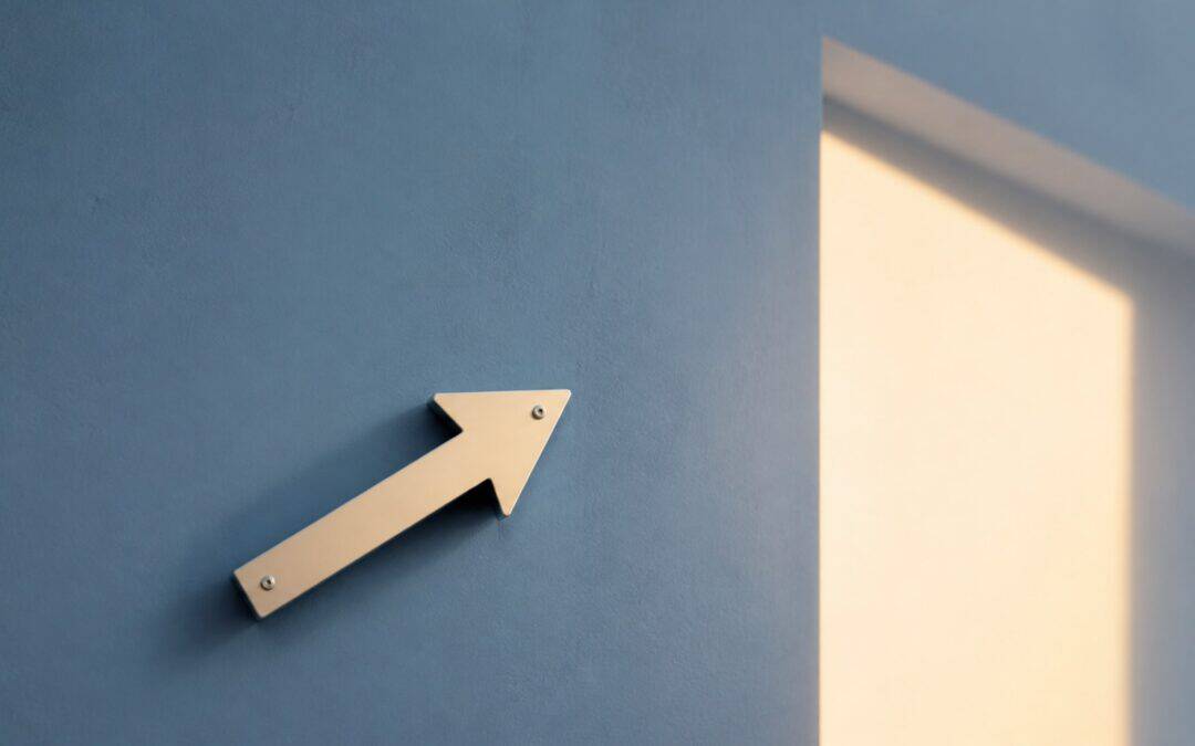 Cream arrow mounted on a muted blue wall pointing toward a warm doorway-shaped patch of light.