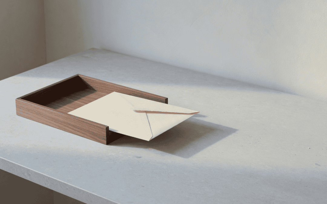 A cream envelope sliding into a dark walnut inbox tray on a pale stone desk.
